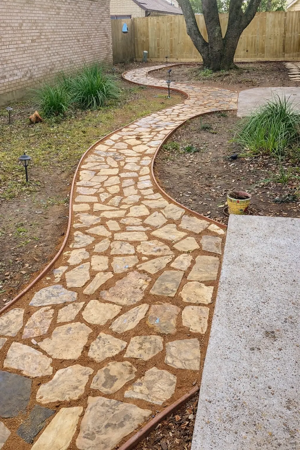 A curving flagstone path with metal edging through a backyard